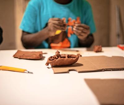 In een opvangcentrum voor asielzoekers in België boetseert een deelnemer een boot. © The Red Pencil